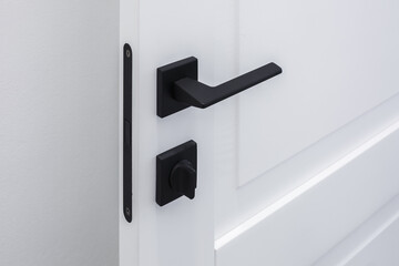 Modern black door handle on white wooden door in interior. Knob close-up elements. Door handle, fittings for interior design - obrazy, fototapety, plakaty