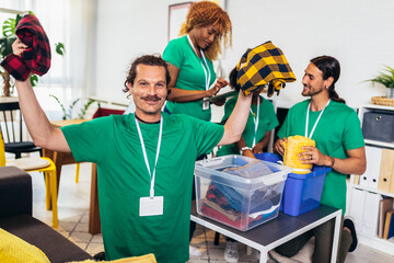 Volunteers putting clothes in donation boxes. Group of young multicultural volunteers in green...