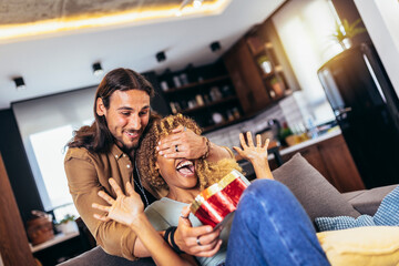 Handsome guy is covering his girlfriend eyes and giving a gift box