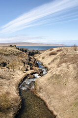 Little mountain stream flowing between rocks and grassy hills towards the fjord near Hvammstangi, Iceland