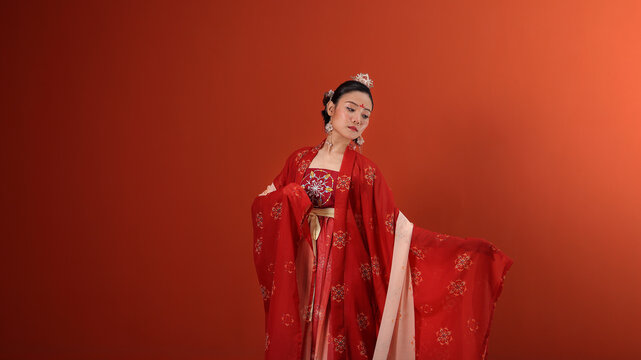 Young attractive Asian woman wearing tadeonal Chinese red hanfu long skirt dress costume scarf hairpin earring indoor on read marron background wall