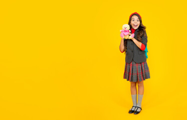 amazed child in school uniform with backpack and toy on yellow background, copy space, september