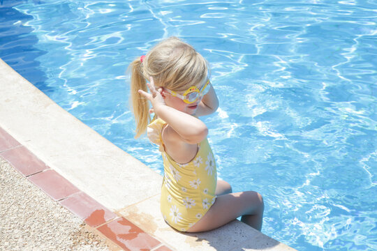 Toddler girl in yellow swimsuit sitting at the edge of pool	