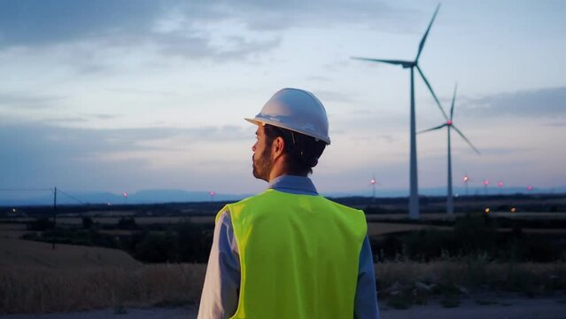 Engineer man from behind observing windmills at night. Renewable energies 