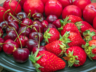 Dark plate full of cherries, strawberries and plums. Selective focus.