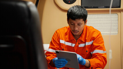 Portrait of Emergency medical technician (EMT) Asian man or paramedic using tablet while sitting in...