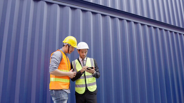 Asian man and Caucasian man Industrial engineer standing and talking about the new project on mobile phone at the transport container warehouse or container terminal