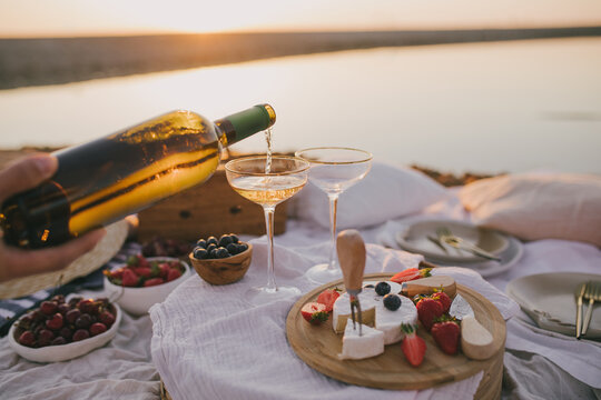 Beautiful romantic picnic with two glasses of white wine, fresh cheese and berries on the beach at sunset.