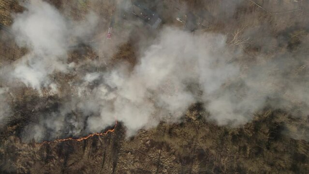 Aerial top-down trucking shot over the wildfire in the suburban area covered by a thick smoke