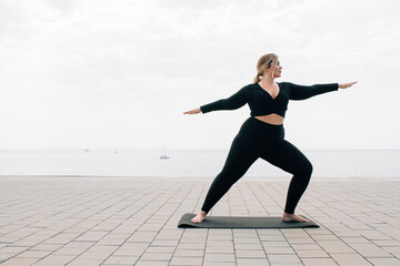 plus size girl practicing yoga in front of the ocean