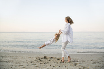 Mother and daughter having fun on the beach. Mother holding girls hands and spinning around. Family outdoor activities concept.	