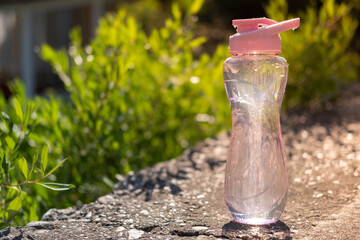 A bottle of water. Reusable plastic water bottle on the background of green grass. Watered from above by raindrops on a hot summer day