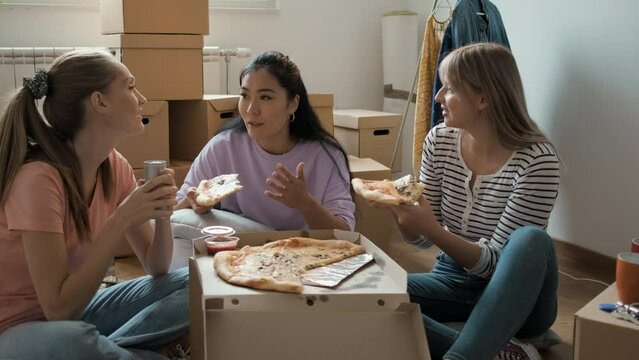 Female friends friends resting and eating pizza after bringing the boxes into the new apartment.