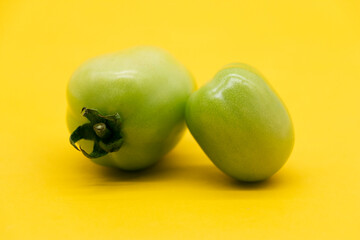 Two green tomato isolated on yellow background.