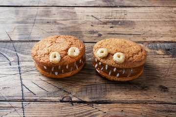Cookies with cream paste in the shape of monsters for Halloween celebration. Funny homemade faces made of oatmeal cookies and boiled condensed milk. copy space