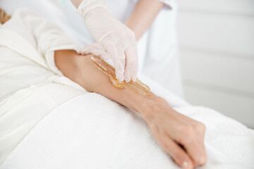 Professional is doing hair sugaring depilation on female hand in cosmetology center