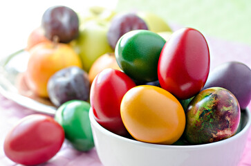 Colored and shiny Easter eggs arranged in white bowl with fresh fruits in background