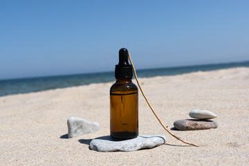 A bottle of dark amber glass with gel or serum with hyaluronic acid on a stone on the sand with a dry twig on the background of the sea. Natural organic cosmetic. Layout of the beauty salon branding.