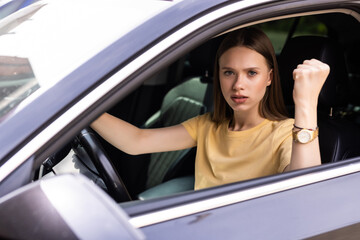 Young woman is driving her car very aggressive and gives gesture with his fist