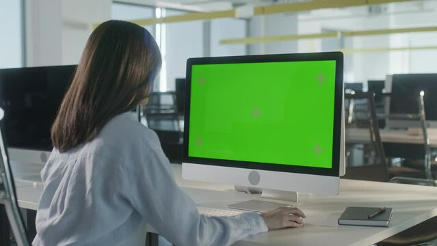Over The Shoulder Shot Of a Business Woman Working In Office Interior On Pc On Desk, Looking At Display Green Screen. Office Person Using Computer With Computer Green Screen, Sitting at Table.