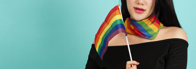LGBTQ woman holding pride flag standing against a blue green background. Asian LGBTQ woman with...