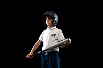 One kid, little baseball player in blue-white uniform leaning to play baseball isolated on black studio background. Concept of sport, achievements, studying, competition