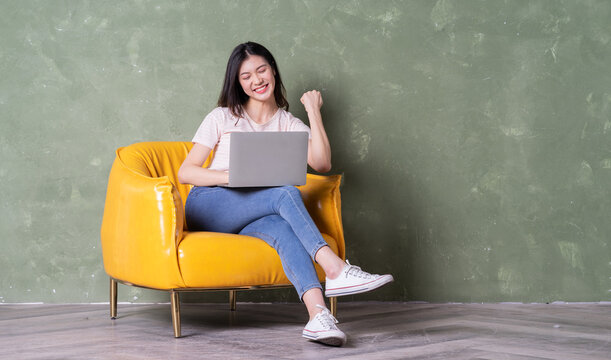 Image of beautiful young Asian woman sitting on yellow armchair