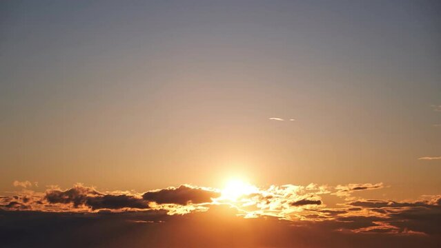 Sunrise among beautiful clouds. Orange sun in the morning sky, timelapse