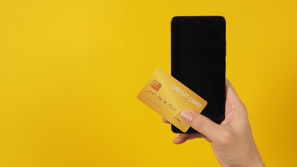 Smartphone with blank screen and gold credit card in man hands with yellow background.