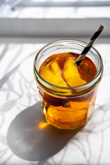 Ein Glas Eistee mit einem Strohhalm auf einer weißen Fensterbank in der Sonne. Licht und Schatten.