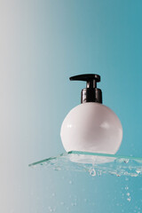 Mockup of a white dispenser with a cosmetic product on glass shelf and falling drops on blue background.