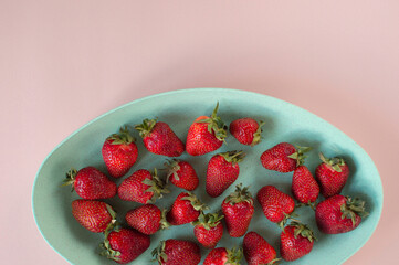 On a pink background there is a green eco cup with red juicy organic strawberries strawberries. Bright red strawberries in close-up