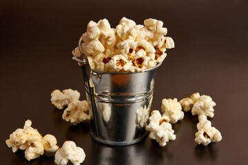 A small bucket filled with popcorn on a black background.
