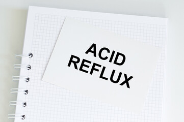 ACID REFLUX text on a card that licks on a blank notepad page on a table