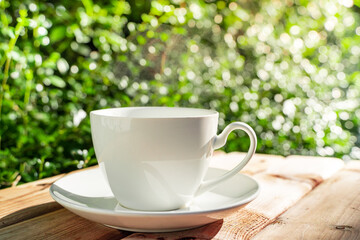 white ceramic coffee mug On the wooden floor, green tree bokeh background in the morning sun in the garden.