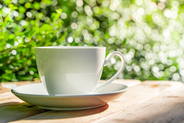 white ceramic coffee mug On the wooden floor, green tree bokeh background in the morning sun in the garden. soft focus.shallow focus effect.