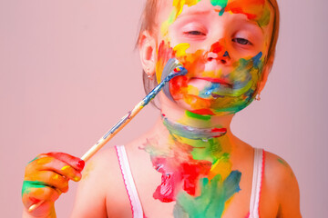 Little cute girl making herself children's makeup with brush and colorful  painted hands. Beauty, leisure, happy childhood and art concept. Close up.