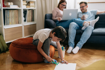 family spending time together at home. boy drawing , mother and father using laptop