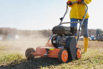 Woman villager is using aerator machine to scarification and aeration of lawn or meadow