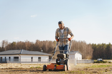 Man using aerator machine to scarification and aeration of lawn or meadow