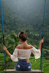 Woman on rope swings with beautiful view on rice terraces in the Bali.