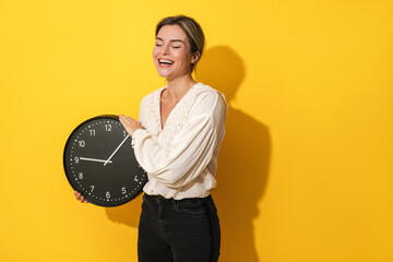 Cheerful woman holding big clock on yellow background