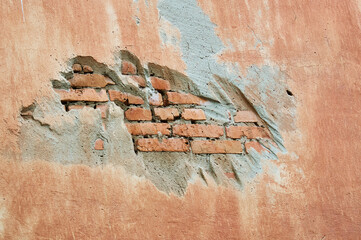 The texture of a building cladding with a piece falling out with a gap on a crumbling brick wall....