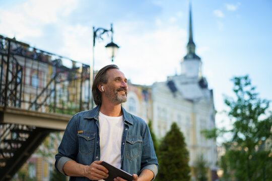 Aged happy men connected on internet with tablet on city background. Beared man in denim shirt in sunny city with pad.