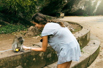 Young female tourist feeding monkey with fruits in Thailand.