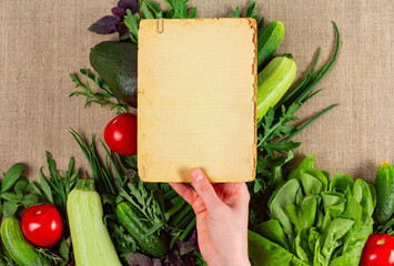 Old vintage paper sheet in hand over the plenty of ripe vegetables. Vegetarian healthy food recipe concept.