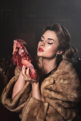 Provocative image of gorgeous wearing wearing fur coat and holding piece of raw beef. Animal rights...
