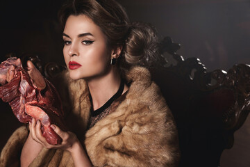 Provocative image of gorgeous wearing wearing fur coat and holding piece of raw beef. Animal rights...