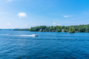 A high-speed white boat with a black awning moves quickly through the water of Laconia Lake (New Hampshire)