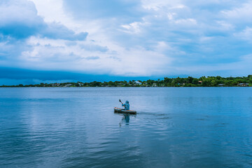 A fisherman in a kayak with a paddle in his hands and a fishing rod lying on the St. Sebastian River in cloudy weather before a thunderstorm.  Florida.